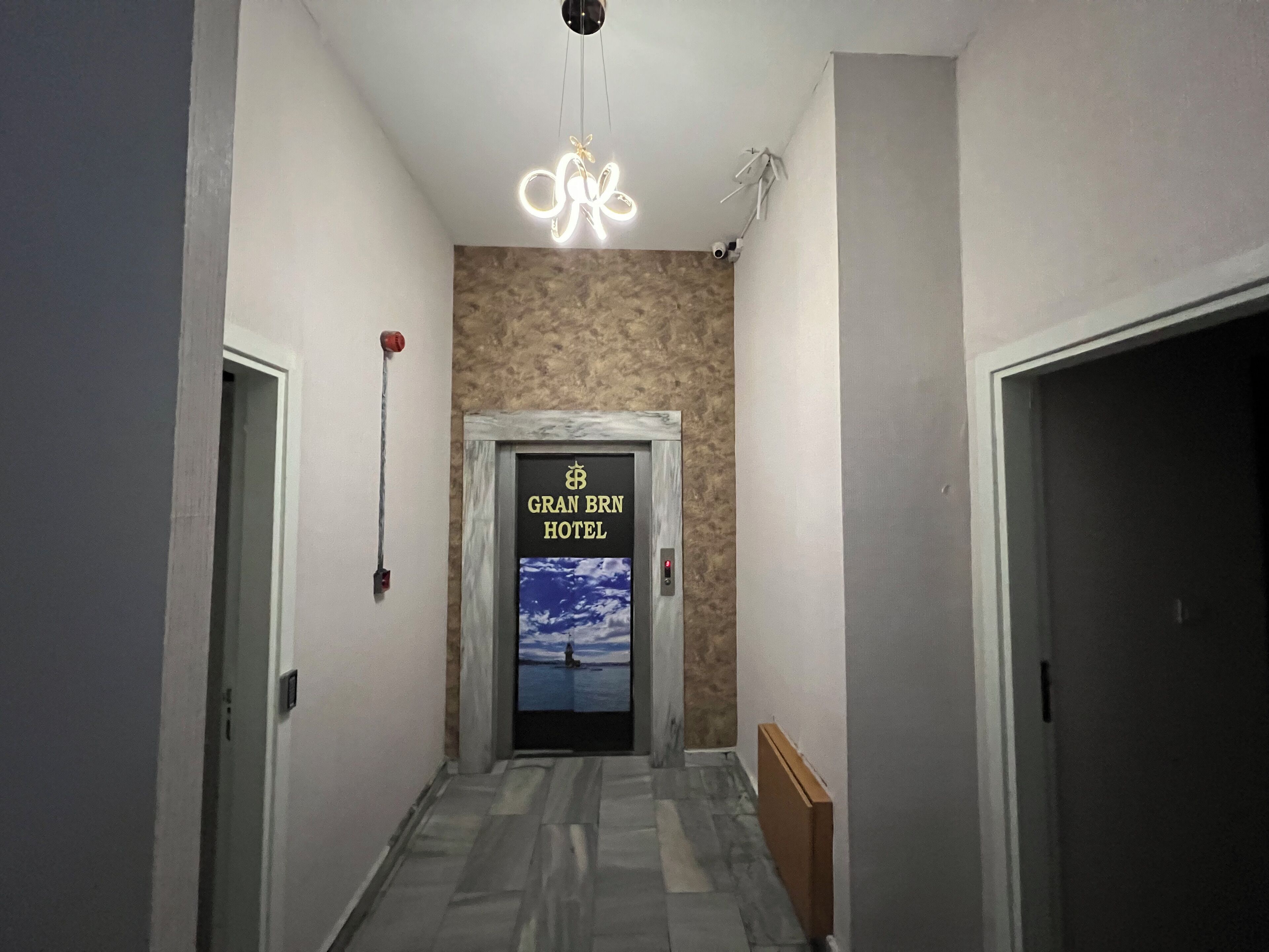 A hotel hallway with a marble floor, a door with a 'Gran BRN Hotel' sign, and a ceiling light fixture.
