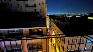 Paisagem urbana noturna com edifícios e vista das luzes da cidade ao longe.