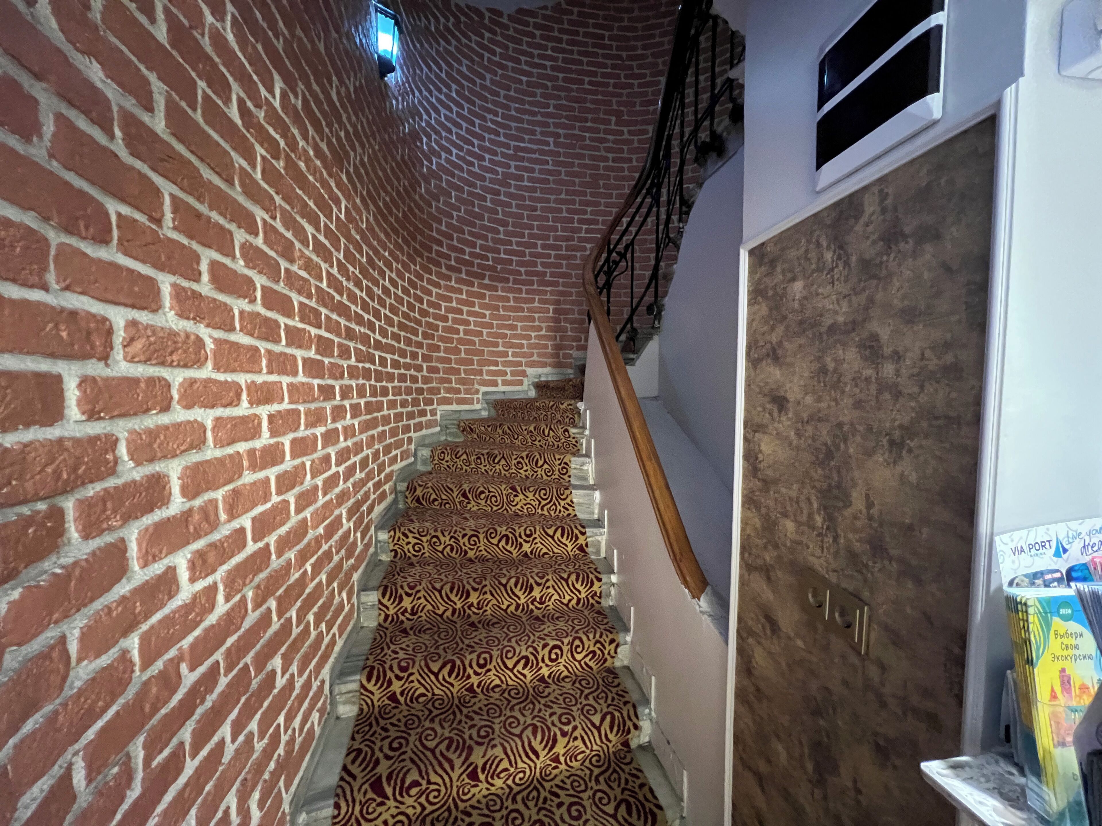 A staircase with patterned carpet, brick walls, and a wooden handrail.