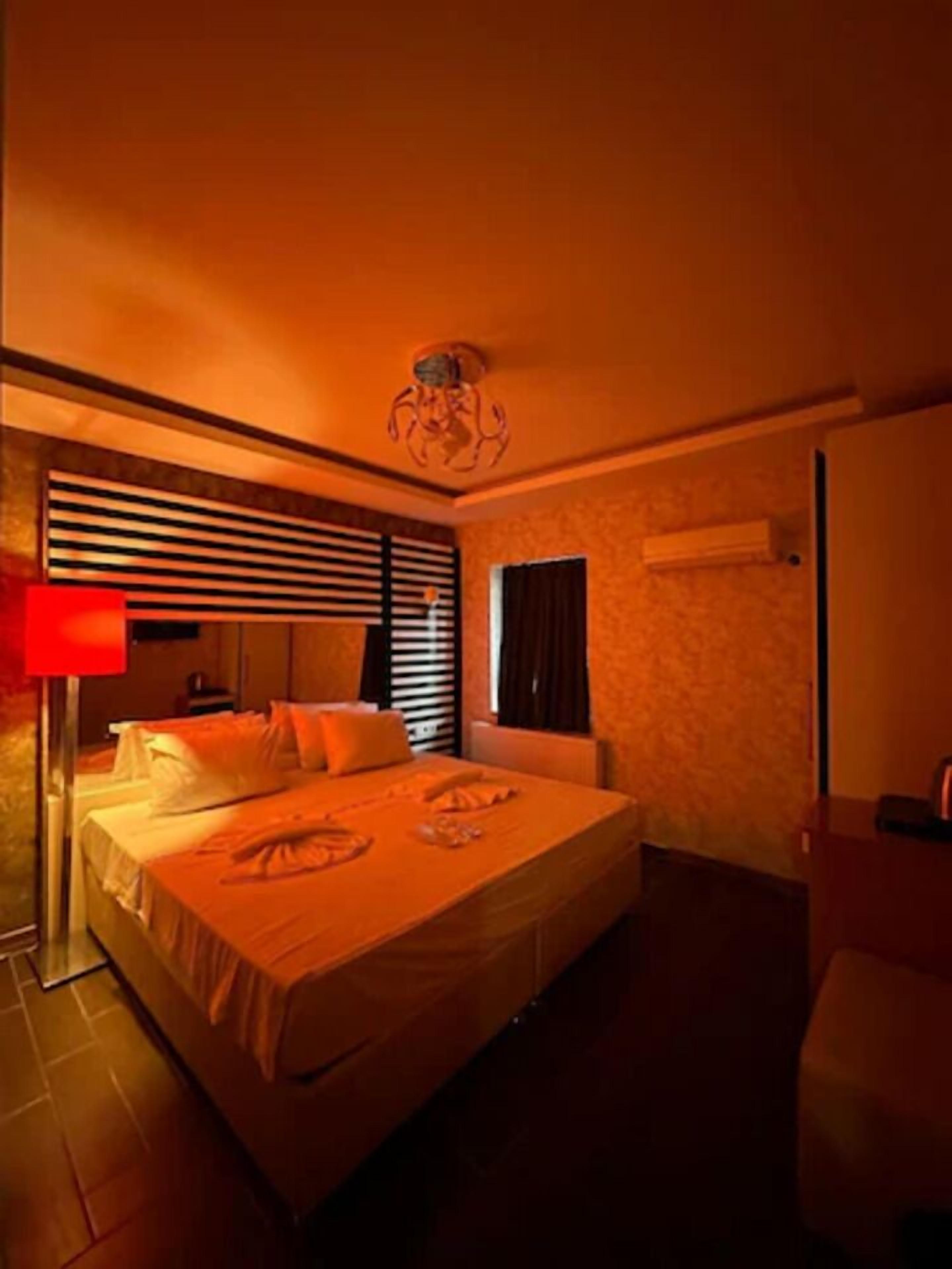 Une chambre d’hôtel avec un grand lit, une table de chevet, une lampe et une fenêtre avec des stores.