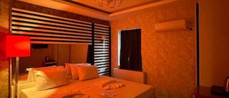 Une chambre d’hôtel avec un grand lit, une table de chevet, une lampe et une fenêtre avec des stores.