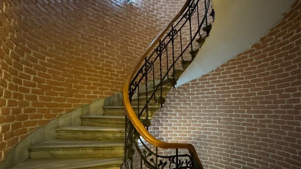 Uma escada em espiral com uma parede de tijolos de um lado e uma parede branca do outro, conduzindo a um andar superior.