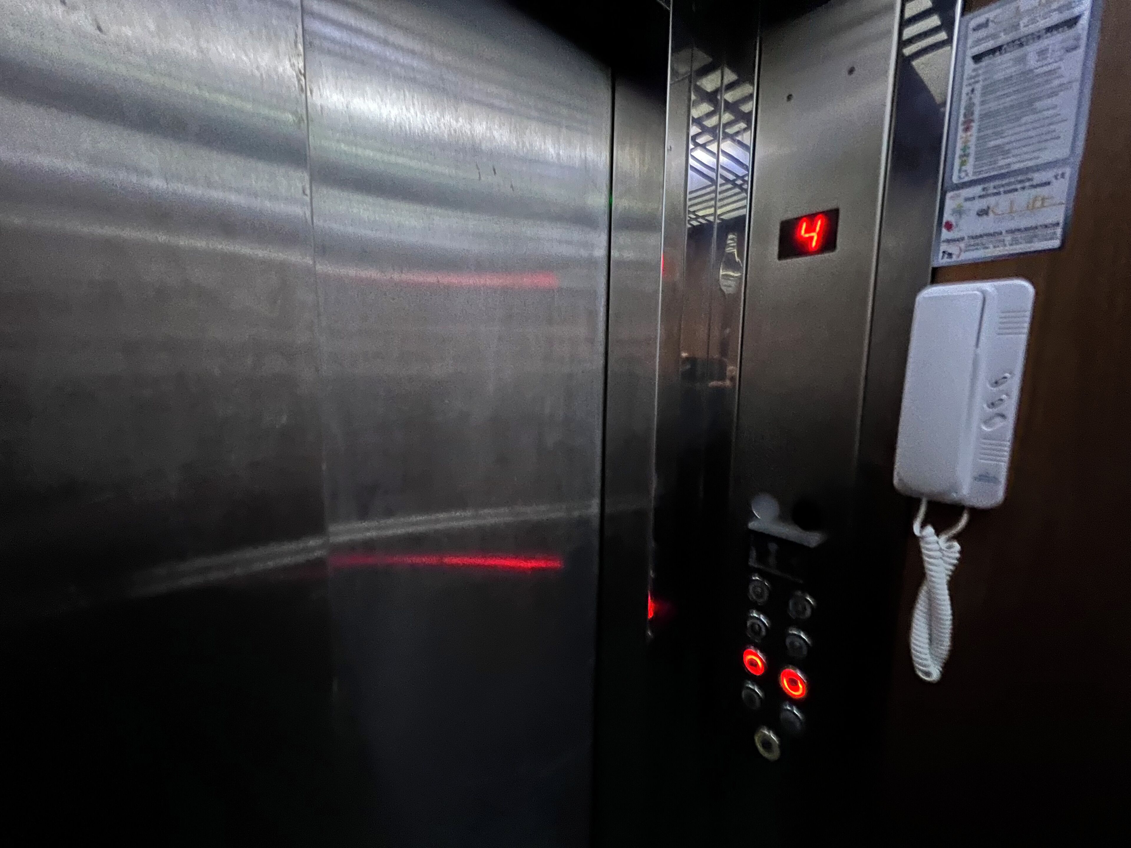 An elevator interior with metallic walls, a digital display showing the number 4, and a phone mounted on the wall.