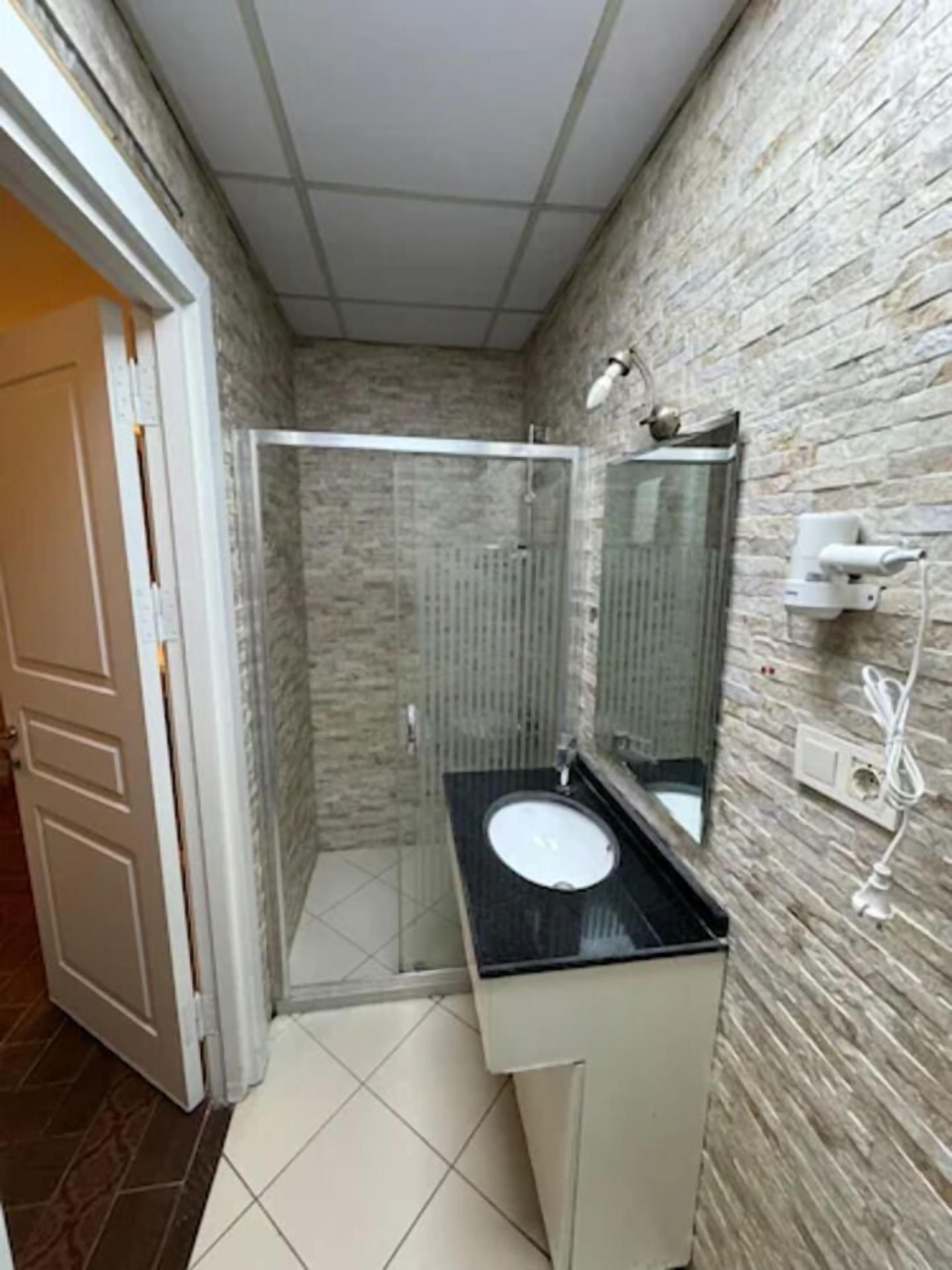 Un bagno con doccia vetrata, un lavandino bianco su un piano di appoggio nero e uno specchio sopra il lavandino.