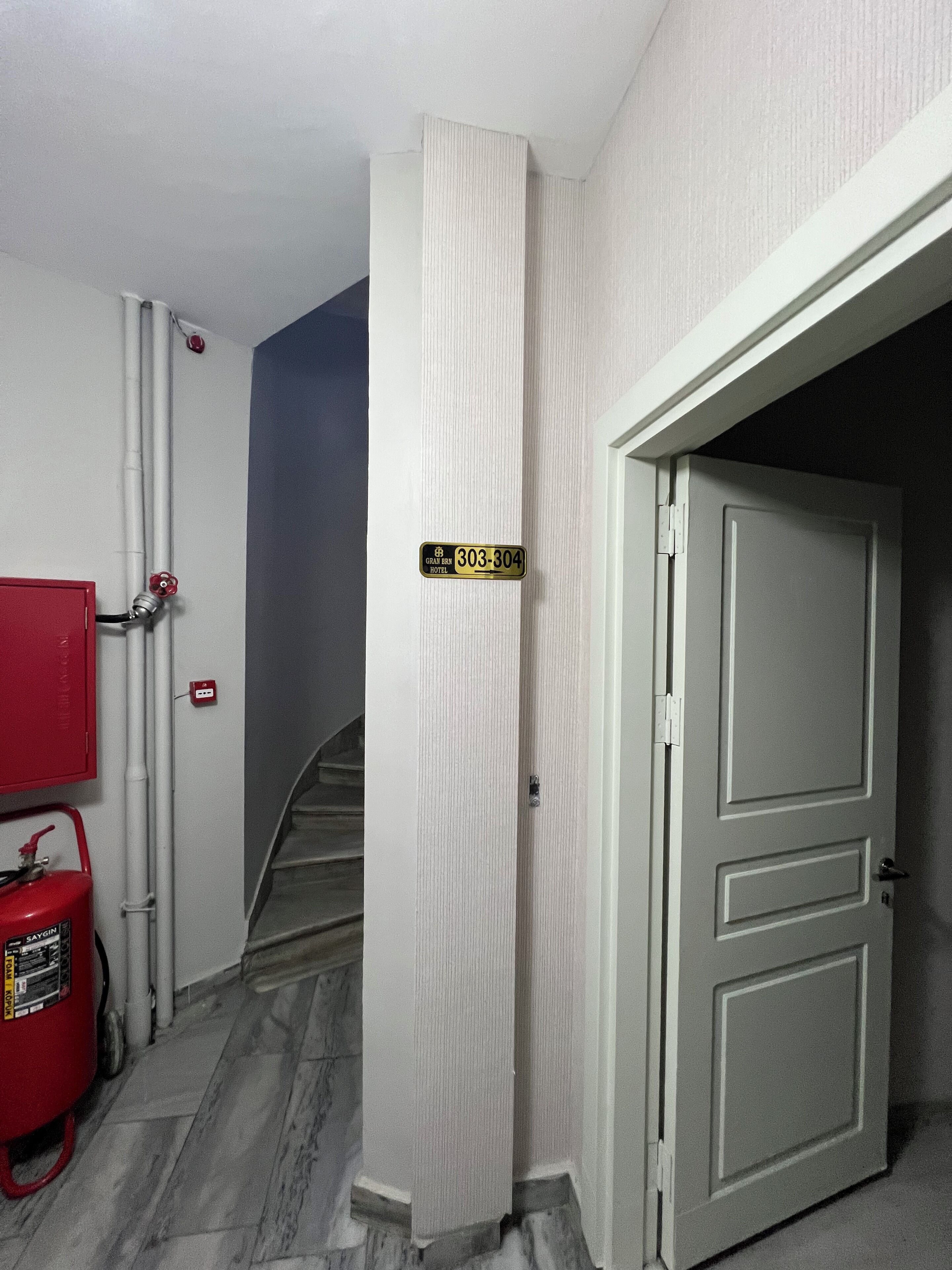 A hallway with a fire extinguisher, a sign with a phone number, and a door leading to another room.