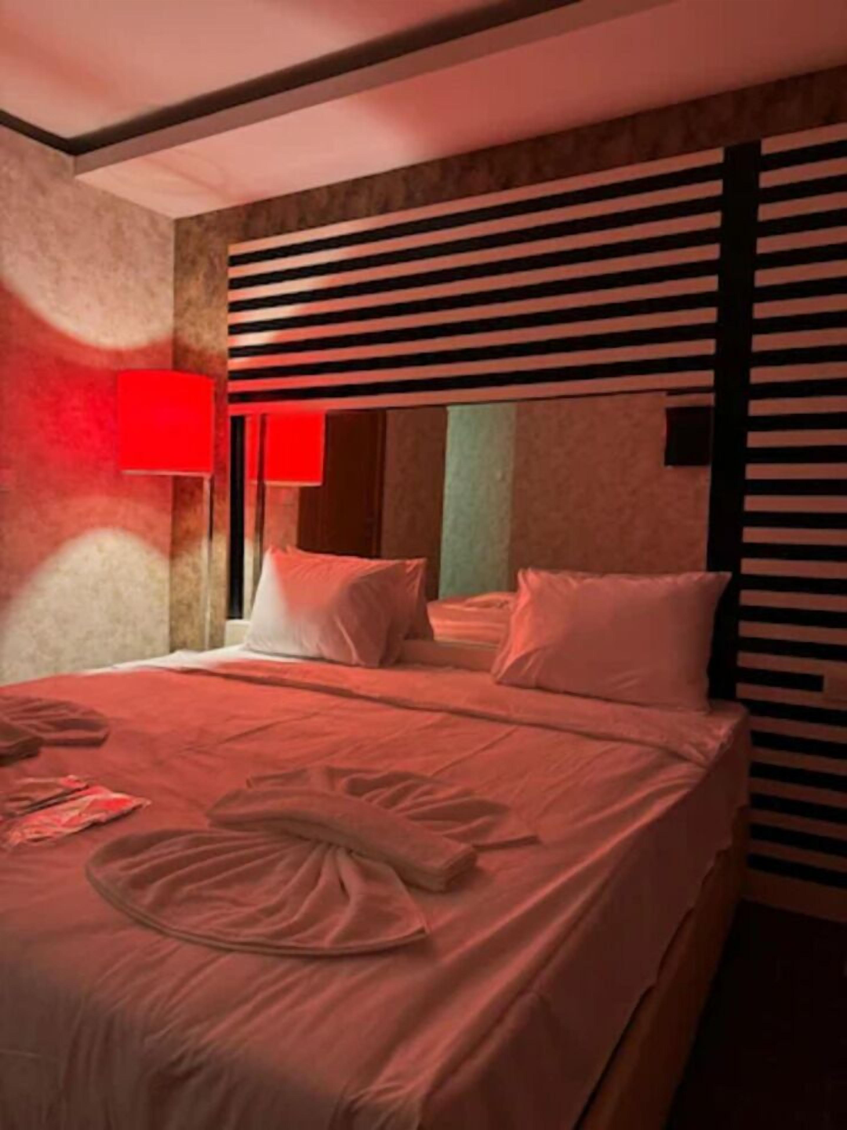 Une chambre d’hôtel avec un lit, des oreillers et un luminaire rouge fixé au mur.