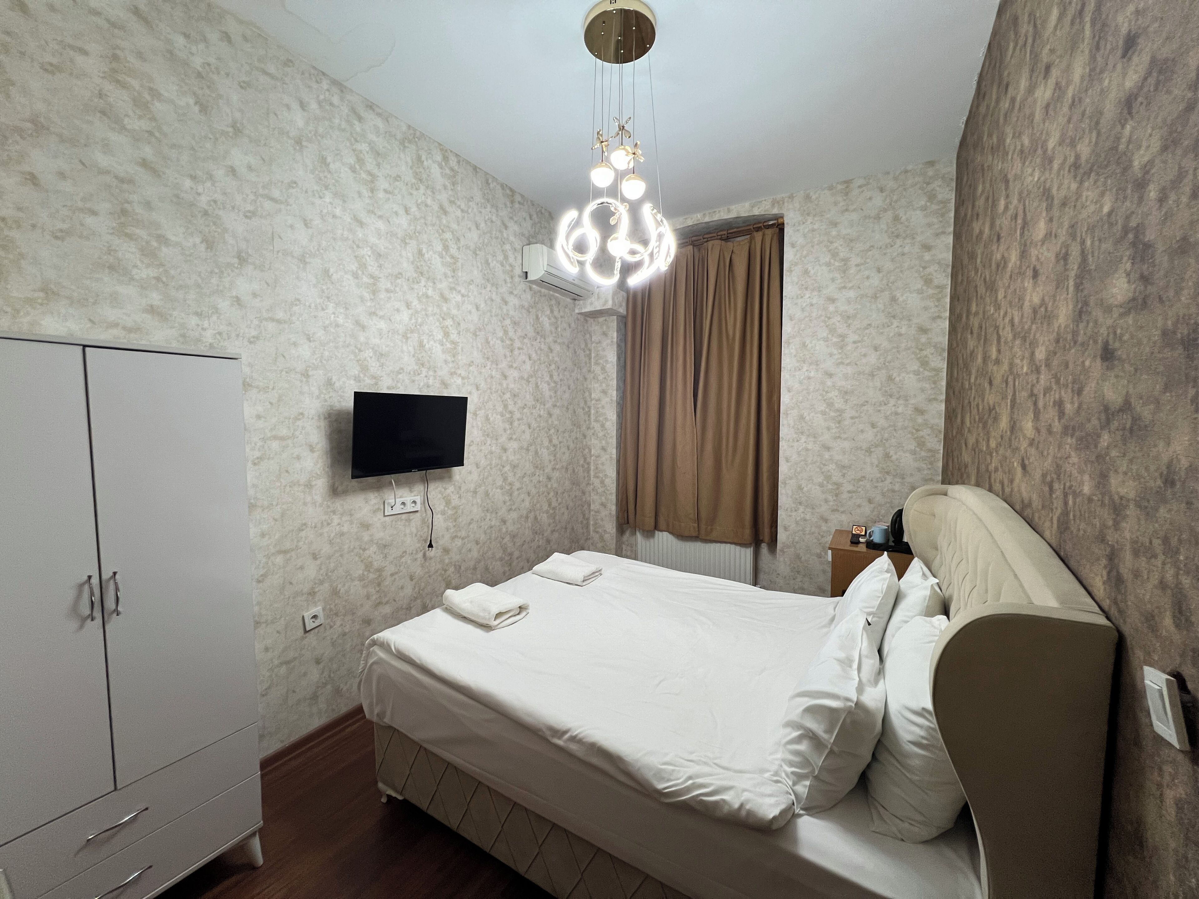 Quarto com cama, guarda-roupa, televisão e luminária de teto.