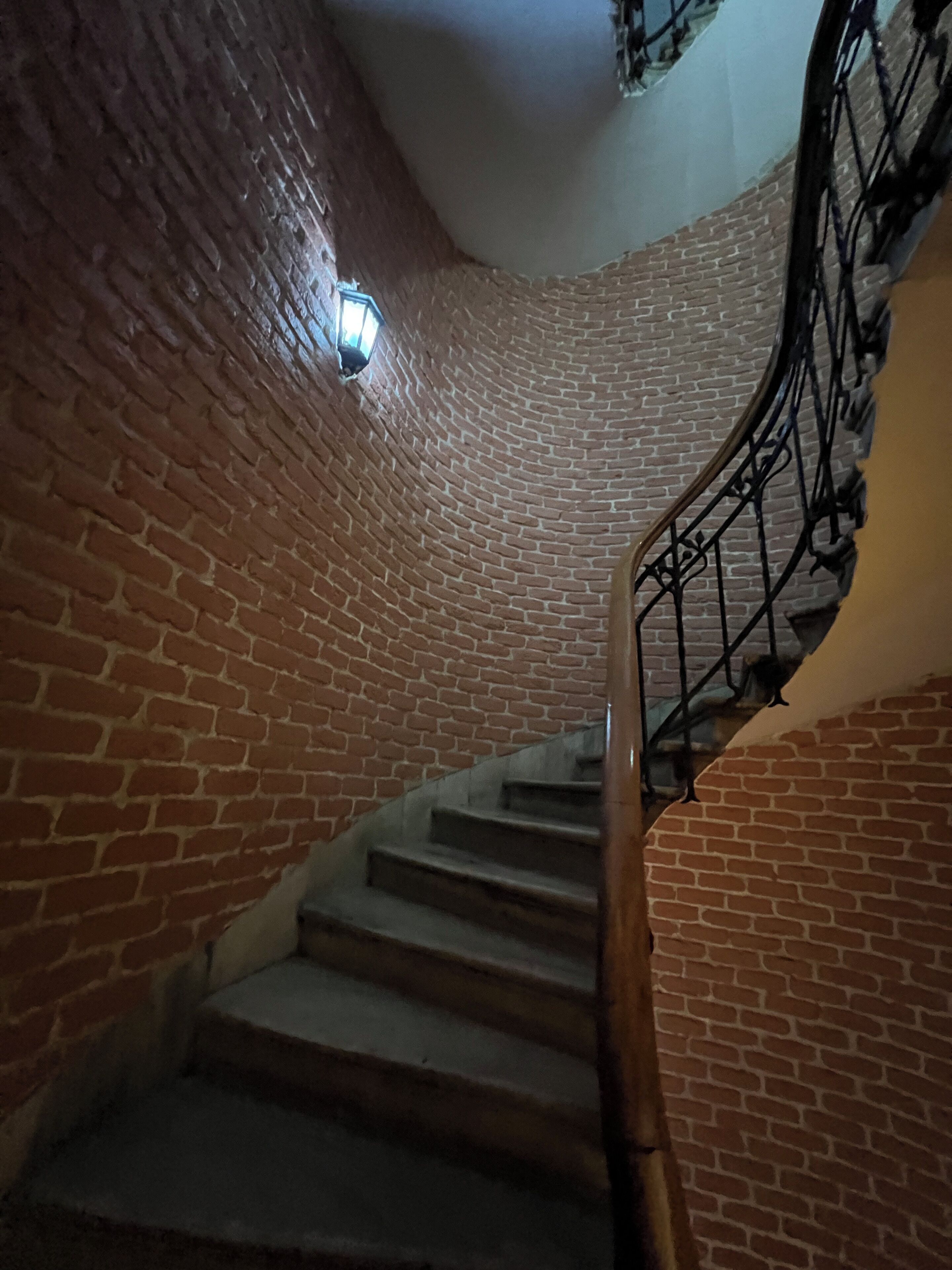A spiral staircase with brick walls and a metal railing.