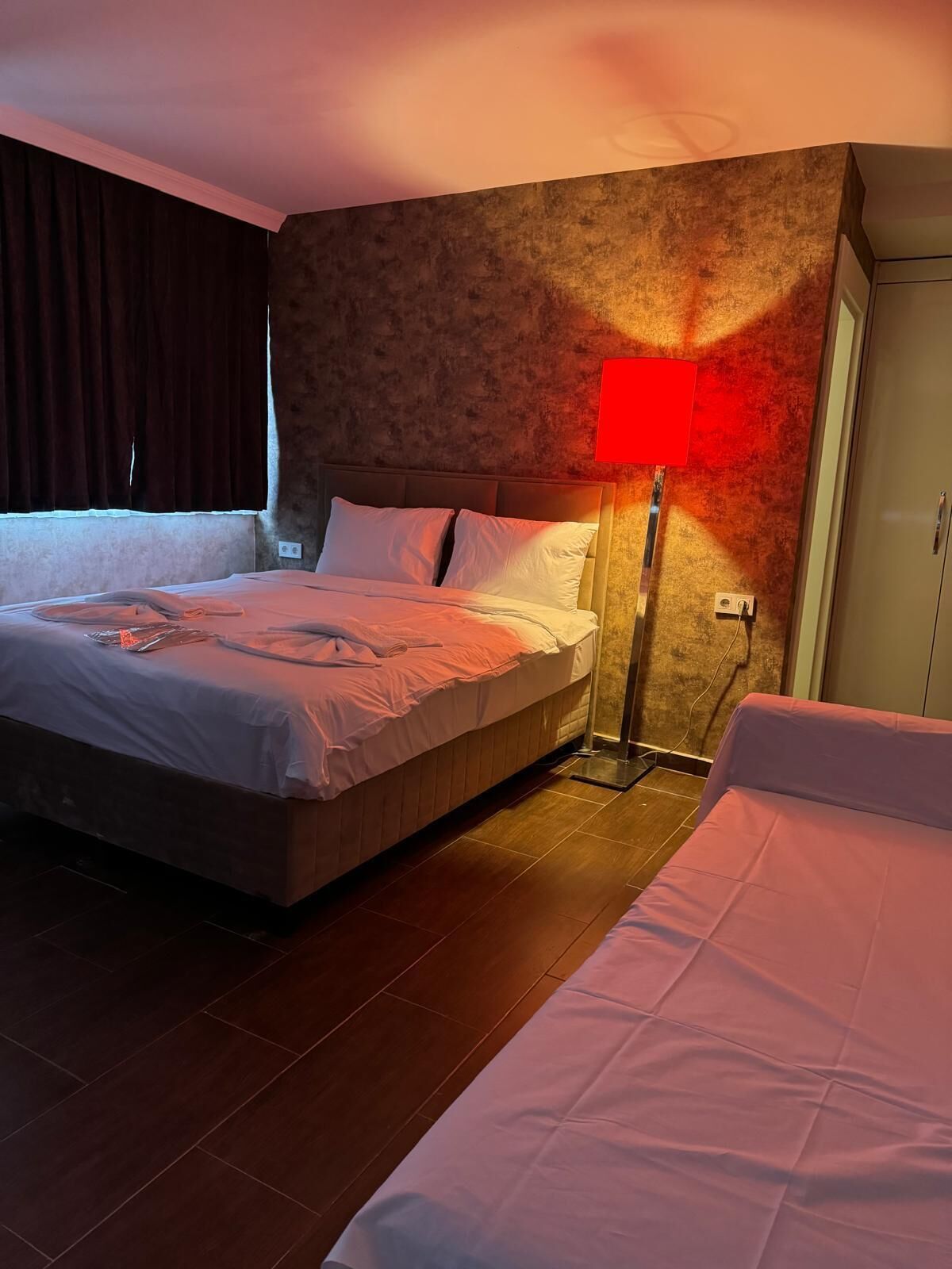 A hotel room with a large bed, a bedside table, a red lamp, and a wardrobe.