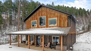 Un chalet rustique en bois, doté d’un porche abrité, de grandes fenêtres et surplombant un paysage enneigé.