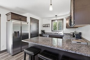 A modern kitchen with a stainless steel refrigerator, granite countertops, and black leather bar stools.
