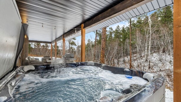 Un bain à remous avec une terrasse en bois et une vue sur une forêt enneigée.