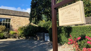 A sign for 'Mead Farm The Barn' indicating self-catering holiday cottages with a gravel driveway and stone building.
