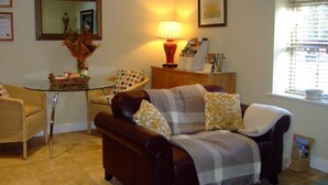 A living room with a brown leather sofa, a glass coffee table, a wicker basket, a lamp, and a window with blinds.