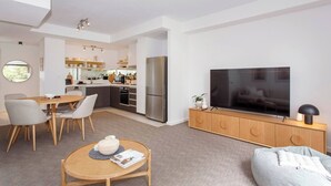 Apartament modern amb zona de menjador, cuina, saló i un televisor gran.