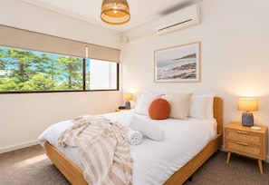 Une chambre moderne avec un grand lit, des lampes de chevet, une fenêtre donnant sur des arbres et un tableau encadré au mur.