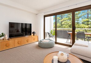 A modern living room with a flat-screen TV, wooden cabinet, grey bean bag, and a round coffee table with a teapot.