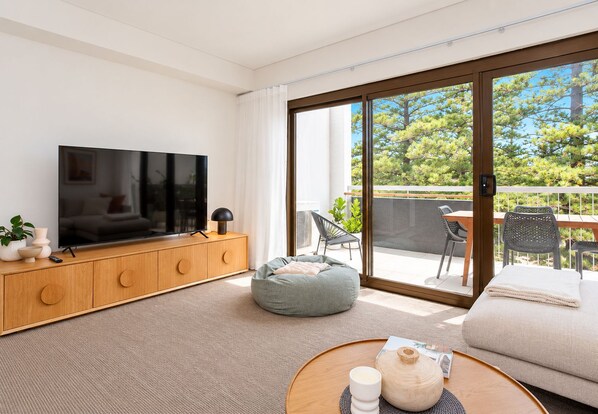 A modern living room with a flat-screen TV, wooden cabinet, grey bean bag, and a round coffee table with a teapot.