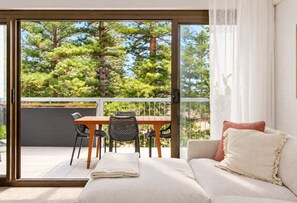 A balcony with a dining table and chairs, a sofa with cushions, and a view of trees.