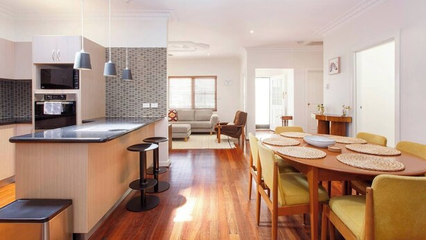 A modern kitchen with a central island, built-in appliances, and a dining area with a wooden table and chairs. - This house is a 2 bedroom(s), 2 bathrooms, located in Fremantle, WA. (Fremantle)