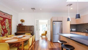 A modern kitchen with a wooden dining table, bar stools, and a refrigerator. - This house is a 2 bedroom(s), 2 bathrooms, located in Fremantle, WA. (Fremantle)