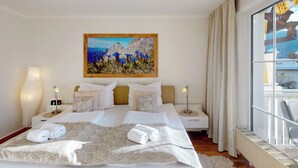 A hotel room with a large bed, two bedside tables with lamps, a painting on the wall, and a view through the window. - Welcome to the cozy holiday apartment Alberta! (Garmisch-Partenkirchen)
