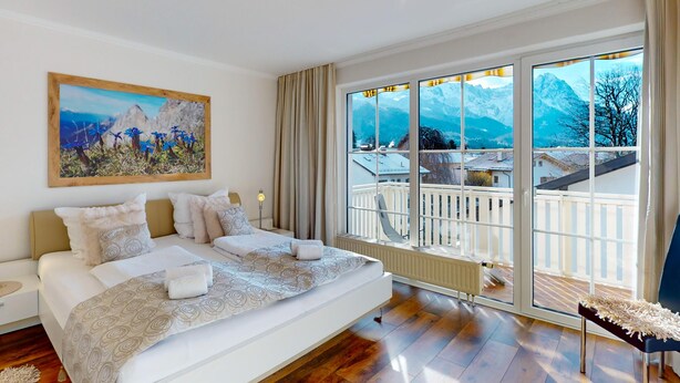 A modern bedroom with a large bed, a view of mountains through large windows, and a balcony with a railing. - Welcome to the cozy holiday apartment Alberta! (Garmisch-Partenkirchen)