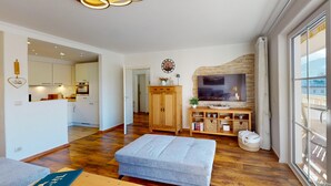 A modern living room with a sofa, ottoman, wooden cabinet, TV, and a stone wall. - Welcome to the cozy holiday apartment Alberta! (Garmisch-Partenkirchen)
