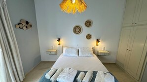 A neatly made bed with white linens and rolled towels, a hanging light fixture, and wall-mounted decor.