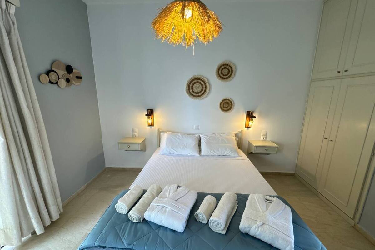 Una cama bien hecha con sábanas blancas y toallas enrolladas, un lámpara colgante y adornos en la pared.