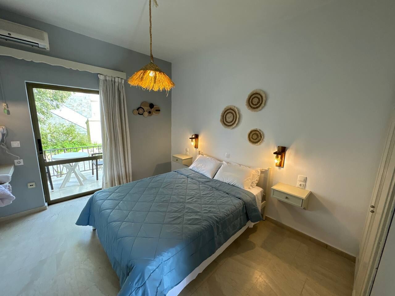 Ein Schlafzimmer mit einem Bett, einem Nachttisch, einer Wandlampe und Blick ins Freie durch eine Schiebetür.