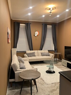 A modern living room with a beige sofa, a round coffee table, and a TV on a stand. - Cozy 1 bedroom suite in tree lined block Near Kings Theatre in Brooklyn, NY. (Brooklyn)