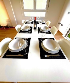 Enjoy meals and social gatherings in this stylish dining area with a long table for four, featuring a wine bottle and fine china.