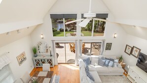 A spacious loft with a high ceiling, a large window overlooking a garden, a white ceiling fan, and a cozy seating area with a sofa and chairs. - New! Lakeview, Charming 3BR, Hot Tub, Firepit, Pet Friendly, WiFi (Littleton)