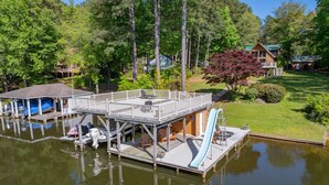 A dock with a covered seating area, a boat, and a water slide. - New! Lakeview, Charming 3BR, Hot Tub, Firepit, Pet Friendly, WiFi (Littleton)