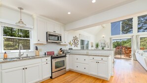 A spacious kitchen with white cabinetry, a stainless steel oven, and a microwave. There is a large window providing natural light and a view of the outdoors. - New! Lakeview, Charming 3BR, Hot Tub, Firepit, Pet Friendly, WiFi (Littleton)
