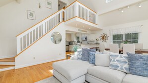 A spacious living area with a light-colored sectional sofa, a wooden staircase, and a kitchen in the background. - New! Lakeview, Charming 3BR, Hot Tub, Firepit, Pet Friendly, WiFi (Littleton)
