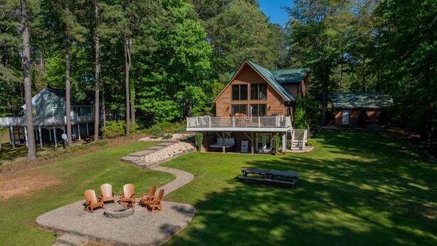 A cabin with a deck, surrounded by a well-maintained lawn and trees. - New! Lakeview, Charming 3BR, Hot Tub, Firepit, Pet Friendly, WiFi (Littleton)