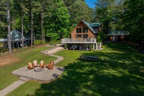 A cabin with a deck, surrounded by a well-maintained lawn and trees. - New! Lakeview, Charming 3BR, Hot Tub, Firepit, Pet Friendly, WiFi (Littleton)