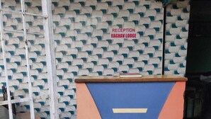 A reception desk with a patterned wall behind it, a sign reading "RECEPTION RAGWAY LODGE", and a tiled floor.