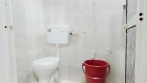 Un baño pequeño y blanco con un inodoro y un cubo rojo sobre una base verde.