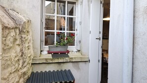 A narrow window with a white frame, a small planter with red flowers, and a metal container with two gas cylinders. - Warm and Authentic! The watchmaker’s house, downtown Crozon (Crozon)