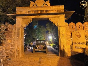 A stone archway entrance to The Cabana Resort, with a jeep parked in front and people visible inside. - THE CABANA RESORT (Vallabhnagar)