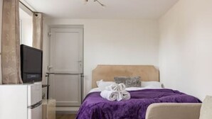 A hotel room with a bed, a television on a stand, a small table, and a door. - Kingston Richmond Lux Brand new Studio (Kingston Upon Thames)