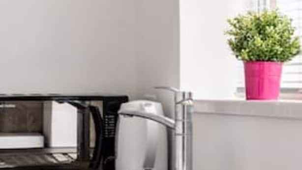 A compact kitchen with a microwave, coffee maker, and a potted plant on the windowsill. - Kingston Richmond Lux Brand new Studio (Kingston Upon Thames)