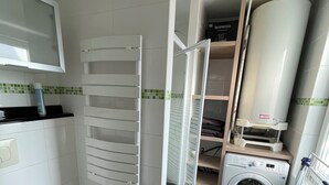 A compact bathroom with a toilet, a washing machine, and a built-in sink.