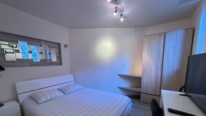 A modern hotel room with a neatly made bed, a desk with a computer, and a TV.