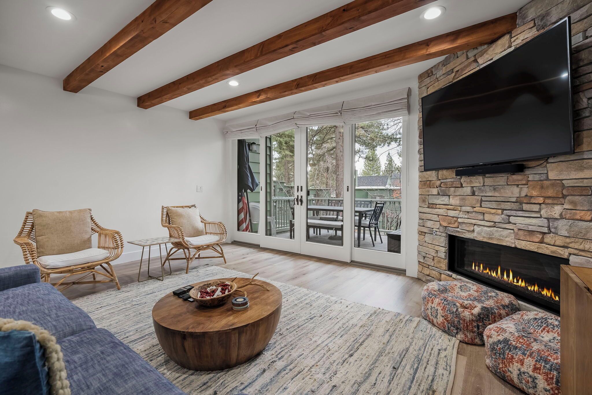 A living room with a stone fireplace, a flat-screen TV, wicker chairs, and a large sliding glass door leading to an outdoor patio.