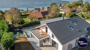 Une maison moderne dotée d’un balcon donnant sur un lac, d’une piscine et offrant une vue sur le quartier environnant.
