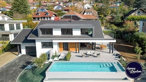 Une maison moderne à deux étages, dotée d’une piscine, de grandes fenêtres et d’un jardin bien entretenu.